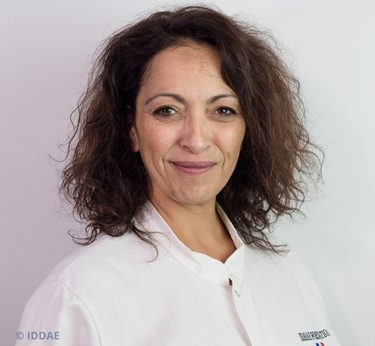 Femme souriante avec des cheveux bouclés, portant une blouse blanche.