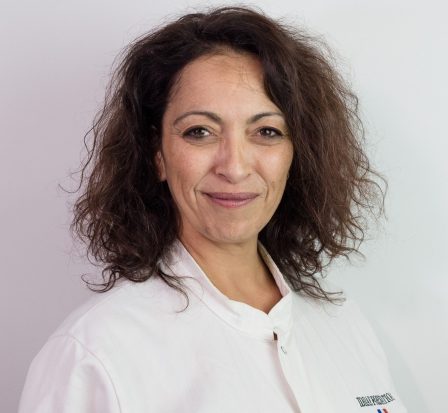 Mejda Jeghi Femme souriante avec des cheveux bouclés, portant une blouse blanche.