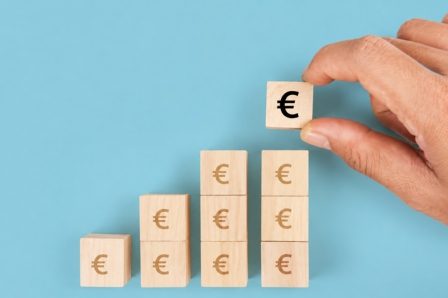 Simplification des process, analyse du ROI projet, approche globale et détaillée, pragmatisme Gain de productivité pour les PME. Main en plaçant un cube avec le symbole euro sur une pyramide de cubes en bois.